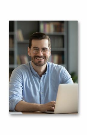 Good-looking millennial office employee in glasses sitting at desk in front of laptop smiling looking at camera. Successful worker, career advance and opportunity, owner of prosperous business concept