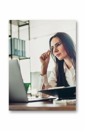 Experienced businesswoman working in an elegant office setting, wearing formal attire and analyzing data on her laptop