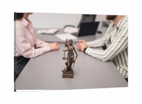 Married couple filing divorce papers in lawyer's office. Statue of Themis close-up in lawyer's office, blurred couple divorce proceedings in background