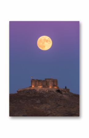 From below picturesque scenery of abandoned aged fortress on top of mountain illuminated by full Moon at night in Toledo