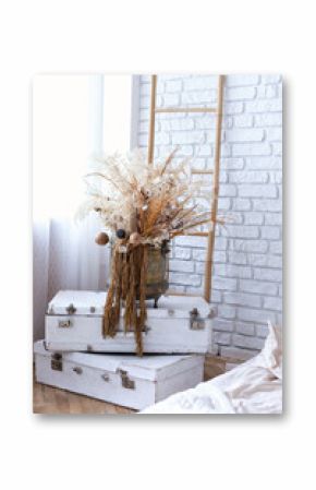 Vintage ancient suitcases trunks in form of tower with vase with bouquet of dried flowers flowers, pampas grass on top and decoratibe stepladder. Interior design room in Boho, shabby chic style. 
