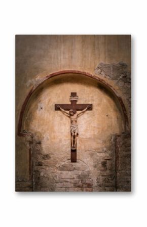 A wooden crucifix depicting Jesus Christ is mounted on an arched, weathered stone wall inside a historic church in Grado, Italy. The worn textures reflect time and reverence.