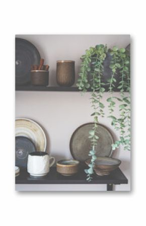 Stylish open space shelves with authentic handmade ceramic dishes, plants and plates. Design interior of cozy kitchen
