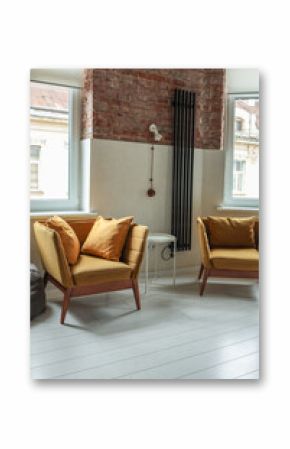 Stylish loft interior with two mustard yellow armchairs, pillows, a white side table, brick and plaster walls, vintage coffee sign, and large windows with natural light