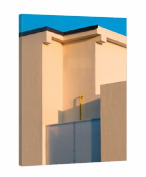 Minimalist architecture detail of modern building facade illuminated by warm sunset light, geometric shapes and clean lines against clear blue sky.