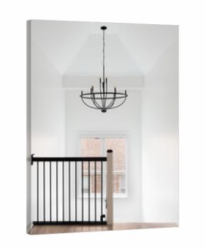 A hallway and staircase with a wrought iron railing, hardwood floor, and chandelier hanging from the tall ceiling.