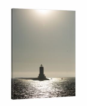 Lighthouse silhouette rising against glowing sunset. Lighthouse form cutting bright sea horizon. Lighthouse shape defining evening coastal scene. Lighthouse presence symbolizing safe navigation.