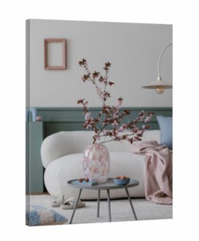 Spring composition of living room interior with mock up poster frame, boucle sofa, round coffee table, glass vase with flowering branches, beige carpet and personal accessories. Home decor. Template.