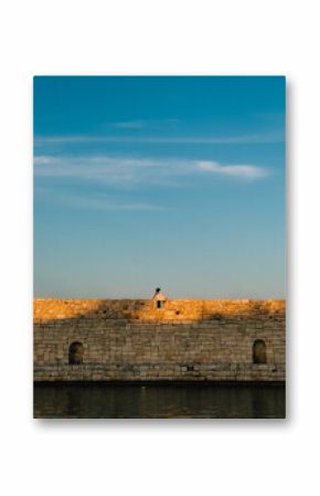 Young woman sitting on ancient city walls of Heraklion, Crete, Greece, enjoying sunset over Mediterranean Sea, beautiful summer evening in historic location. Young woman sits atop ancient city walls