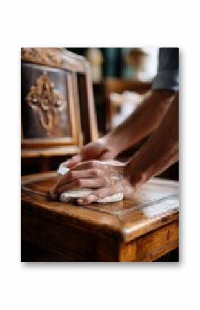 Hands cleaning a vintage wooden chair in a cozy interior space during the afternoon