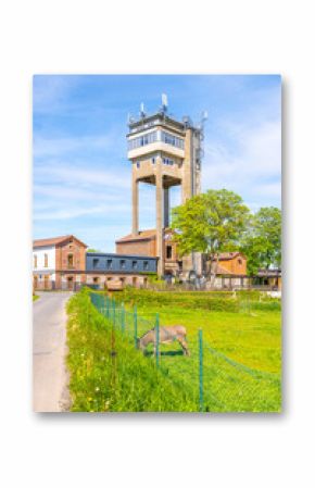 Discover the Rudolfka lookout tower, a former mining tower located in Bohutin, Czechia. The structure stands tall against a clear blue sky, surrounded by green grass and historic buildings.