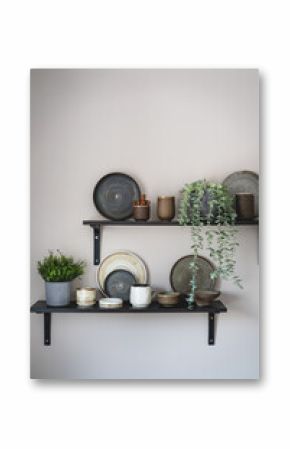 Stylish open space shelves with authentic handmade ceramic dishes, plants and plates. Design interior of cozy kitchen