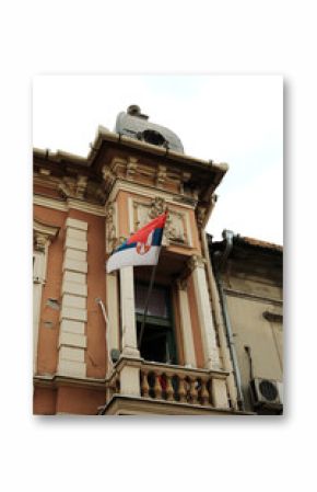 Historic building with a Serbian flag hanging from a balcony in Sombor, Serbia. Patriotic and cultural city scene.