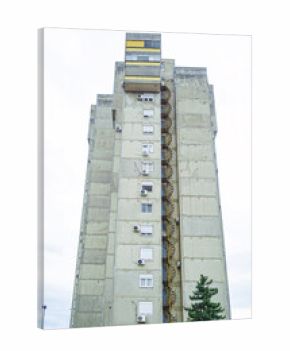 A vertical photo of the side facade of a tall apartment building in the Bratlism style: a gray concrete wall with windows and a spiral fire staircase. Yugoslav architectural heritage in New Belgrade.
