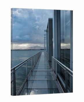 Modern Architecture Walkway Over Water - A metal and glass walkway with industrial design leads over water, reflecting the sky and clouds with a futuristic feel.