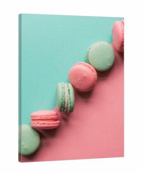 Diagonal line of pink and teal macaron cookies on colorful background.
