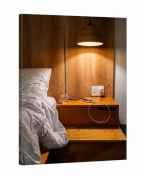 Empty bed with white pillow and sheet next to wooden nightstand and lamp.