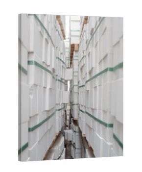 Stacks of cardboard boxes arranged in tall rows forming narrow aisle in warehouse storage area, boxes featuring green bands and wooden pallets supporting upper layers