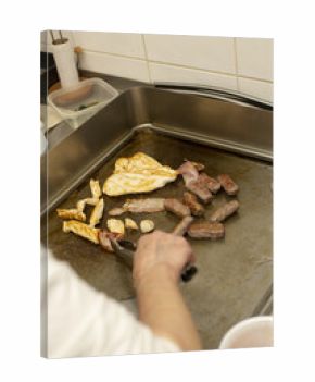 A person is carefully grilling a variety of cuts of meat on a flat cooking surface located in a kitchen
