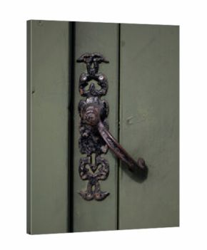 An old, ornate, dark metal door handle and escutcheon plate are mounted on a weathered, light green wooden door, showing signs of rust and age.