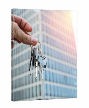 Real Estate Keys Held by Hand in Front of Modern Office Building. Close-up shot of a hand holding several metal keys in front of a sleek modern glass skyscraper