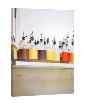 Colorful bottles with various liquids displayed on a shelf in a bright cafe setting