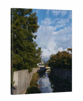 Concrete canal, storm clouds, overhead power lines, water reflection and riverside trees in an urban drainage channel. Empty suburban scene with moody sky for infrastructure or environment study.