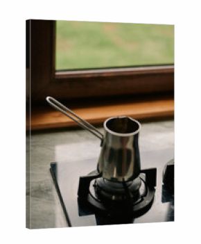 Closeup of a small saucepan resting on a gas burner in a kitchen, metal surface reflecting light, portraying a simple home cooking scene