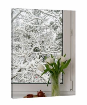 Window view of trees covered in snow with a vase of flowers indoors