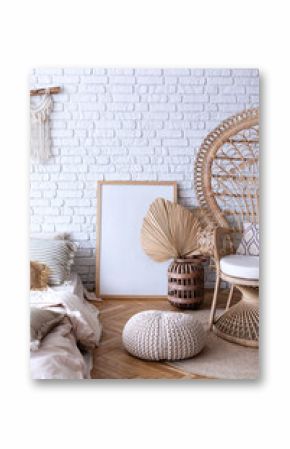 Rattan peacock chair in room with boho decor. Cozy modern stylish interior design bedroom with bamboo armchair, vase with dried leaf, large frame poster, carpet, macrame panel on white brick wall.  