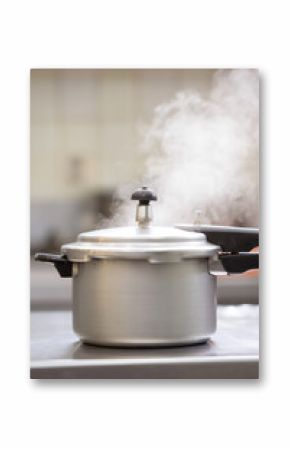 Metallic pressure cooker emitting steam on a kitchen counter. The steam is visibly escaping from the top valve, indicating active cooking. 