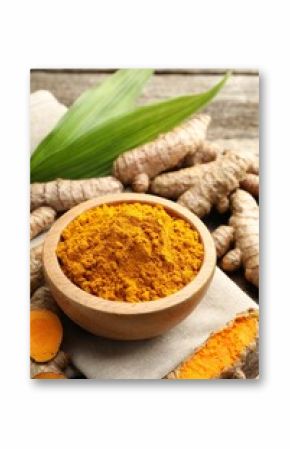 Turmeric powder in bowl, roots and leaves on table, closeup