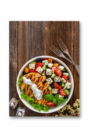Grilled sliced chicken breast and Greek salad on wooden table 