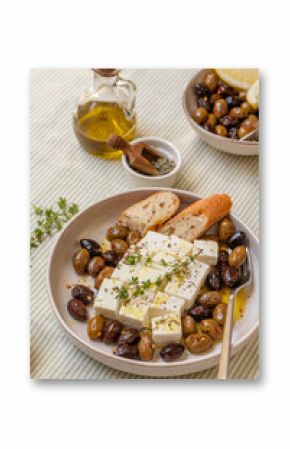 Freshly prepared feta cheese served on a plate with assorted olives, garnished with herbs and lemon slices and  crusty bread, traditional Greek or Italian food, Mediterranean diet