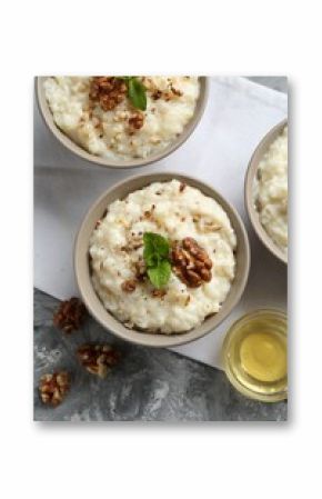 Delicious rice pudding with walnuts, mint and honey on grey table, flat lay