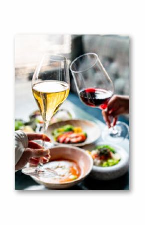 Two people clinking glasses of white and red wine over a table with various dishes, creating a celebratory and elegant dining atmosphere