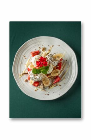 Vanilla ice cream with whipped cream, bananas, strawberries, and mint, served on a white plate with a red edible flower. Refreshing summer dessert with vibrant colors.
