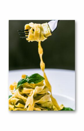 Fituccini al pesto on a white plate and a fork with spaghetti wound on a gray background. Vertical photo. Space for text.