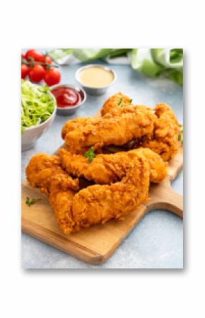 Chicken tenders served on a wooden board with salad and sauces