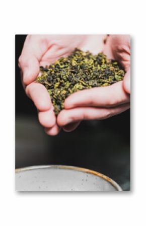 Hands holding loose dried green tea leaves above a ceramic bowl. Natural texture and organic look, ideal for wellness, beverage, or healthy lifestyle themes.