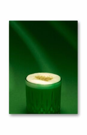 Pistachio latte close-up with thick foam and nut garnish on deep green background. Concept of beverage photography, cafe branding, winter menu, cozy stylish drinks.