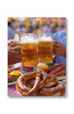 Group of friends toasting with large beer mugs at a festive outdoor gathering, surrounded by delicious pretzels and various foods on a vibrant table setting