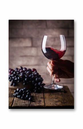 Red wine glass in a men hand and ripe grapes on wooden background