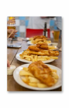 Fish and Chips served on plate, with blurred background of people holding beer glasses