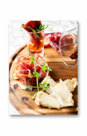 Rustic wooden board with assorted cured meats, cheese, nuts, and dried tomatoes in a glass, perfect for gourmet dining or charcuterie presentations.