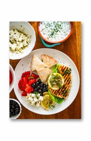 Greek cuisine: grilled chicken breast with lemon, pita bread and greek salad on wooden table 