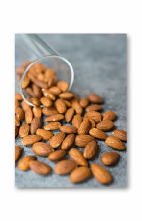 A glass jar spills fresh almonds on a gray stone surface, showcasing their natural texture.