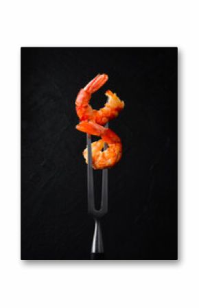 Grilled shrimp on a metal barbecue fork. On a black slate background.