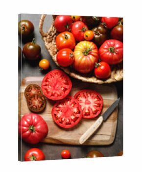 A variety of fresh, ripe tomatoes on a wooden cutting board. A wicker basket contains different colored tomatoes. The scene captures a rustic, farm to table aesthetic. Harvest and cooking concept.