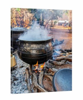 african traditional cooking outdoors in the open fire kitchen on cauldron three legged pot, boiling meat stew